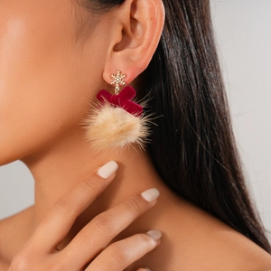 Detail of winter earrings with gold snowflake, burgundy velvet bow and beige fur ball