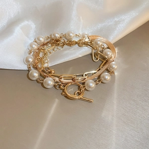 Close-up of layered gold alloy chains and white faux pearls with an OT buckle clasp