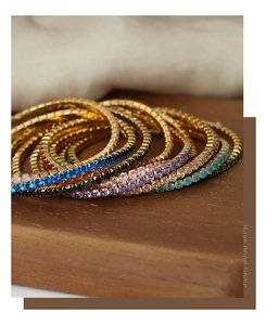 Close-up of gold-plated bracelets with colorful cubic zirconia on a wooden stand