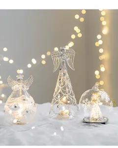 Three glowing glass angel figurines with silver glitter details on a plush white base