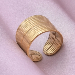 Detailed macro shot of a wide golden textured ring on soft pink silk background