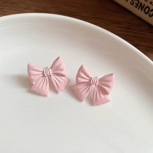 Macro shot of sweet pink bow stud earrings on a white ceramic plate with wood background