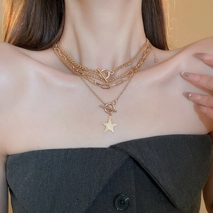 Detail of layered gold Y2K necklaces with star pendant and decorative OT toggles