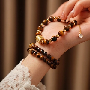 Tiger eye stone beaded bracelet with golden metal charms and crystal pendant on wrist