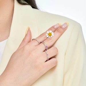 Detailed view of colorful zircon stackable rings on finger with a daisy flower accessory