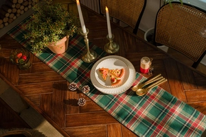 Close-up of red and green plaid table runner on wooden table with festive decoration
