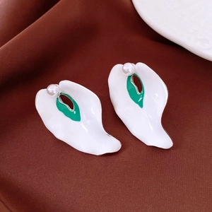 Detail of artistic leaf-shaped earrings with white enamel and centered pearl accent