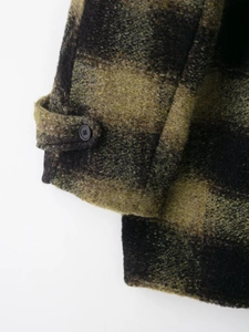 Close-up of the dark green plaid wool coat sleeve with black button and woven texture