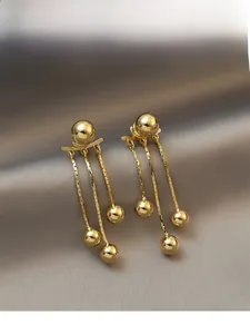 Detailed shot of golden tassel earrings with three metal chains on silk fabric