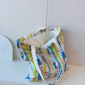 Sac fourre-tout en toile à fleurs avec rayures bleues posé sur une table blanche épurée