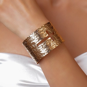 Detail of gold hammered metal cuff bracelet with hollow cross design on white silk