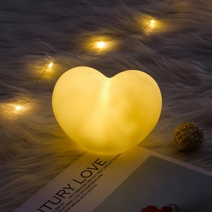 Close-up of heart-shaped night light with warm yellow glow on a white plush rug