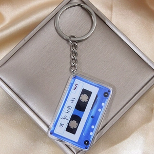 Retro blue acrylic cassette tape keychain on silver gift box with gold silk background