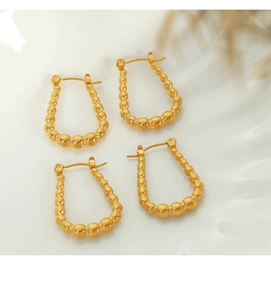 Close-up of golden geometric U-shaped earrings with intricate beaded texture