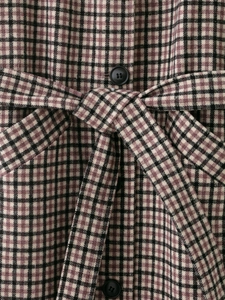 Detail shot of brown plaid coat showing woven texture, waist belt, and black round buttons