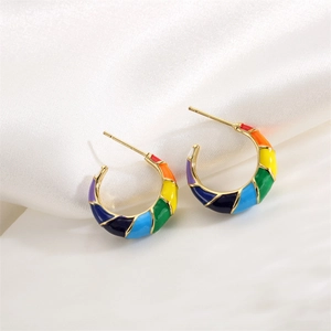 Detailed macro view of rainbow enamel gold C-shaped earrings on white silk fabric