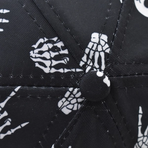 Close-up of the black baseball cap top button showing white skull hand bone print
