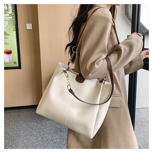 Close-up of large cream tote bag with brown leather straps and gold chain detail