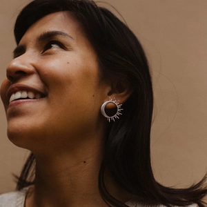 Close-up of silver sun-shaped stainless steel earrings worn by a model