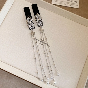 Detail of silver hollowed charms, white pearls, and tassels on a black velvet headband
