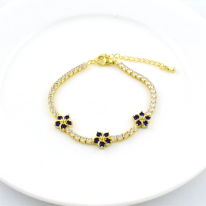 Adjustable gold bracelet with white zircons and blue flower charms on a white plate