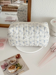 Close-up of quilted floral makeup bag featuring vertical stitching and a white ribbon bow