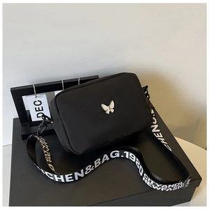 Detail of silver butterfly emblem on black nylon crossbody bag with wide lettered strap