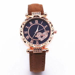 Detail of rose gold watch face with diamond heart accent and Roman numerals on brown strap