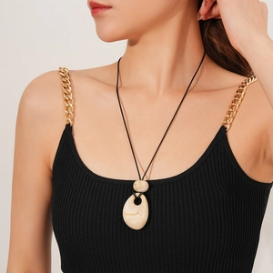 Detail of wax cord necklace with beige bead and teardrop resin pendant on model