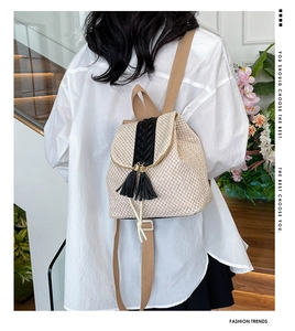 Straw backpack with black fringe tassels and drawstrings shown on a model