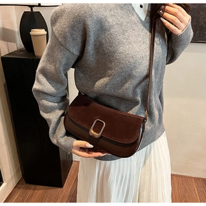 Detail of dark brown suede patchwork shoulder bag with elegant metal buckle on a model