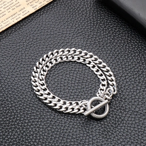Détail d'un bracelet gourmette argenté à double couche avec fermoir OT sur fond sombre