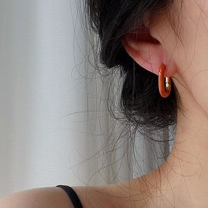 Close-up of minimalist orange resin hoop earrings with 18k gold plated clasp on model