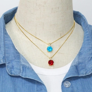 Detail of layered gold necklaces featuring round ruby red and sky blue zircon pendants