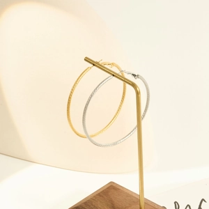 Textured gold and silver hoop earrings with intricate diagonal faceted carving on display