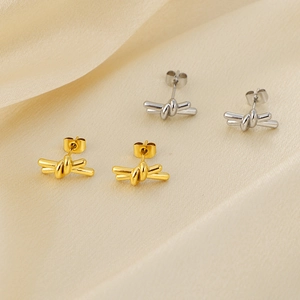 Elegant gold and silver knot stud earrings displayed on champagne satin fabric texture