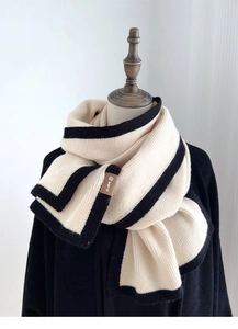 Close-up of beige knitted scarf with black trim and brand tag on a mannequin