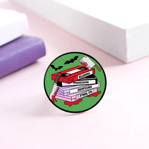 Macro shot of horror movie enamel pin featuring VHS tapes and a bloody slasher knife
