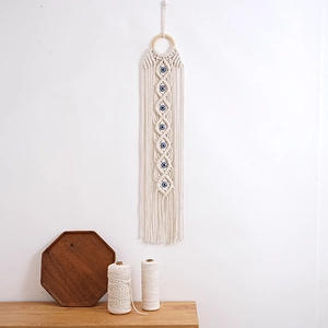 Woven cotton wall hanging with blue Evil Eye patterns and fringe on white background