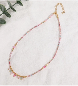 Macro shot of colorful beaded necklace with pink, blue, and green stones on white fabric