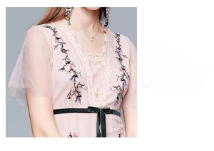 Détail d'une robe en dentelle rose avec broderie florale et nœud en velours vert
