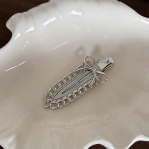 Detailed view of a silver metal ribbon bow hair clip with chains in a shell tray