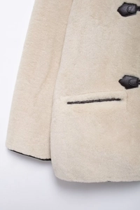 Dettaglio cappotto beige in ecopelliccia con chiusura in pelle nera e texture morbida