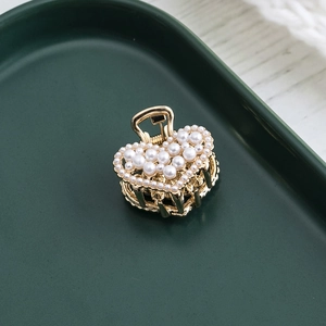 Elegant gold heart hair claw clip with white pearls on a minimalist green tray