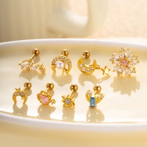 Close-up of gold ear studs with zircon stars, moons and flowers on a ceramic tray