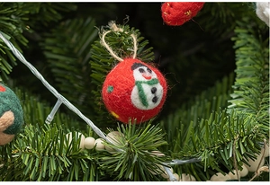 Close-up of a handmade red wool felt Christmas ball with snowman pattern on a pine branch