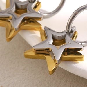 Detailed view of interlocking gold and silver star hoop earrings on a beige stand