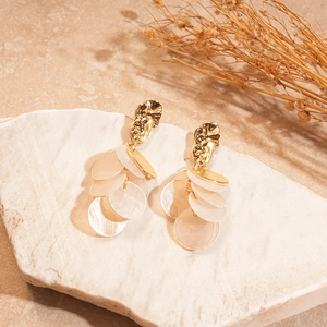 Close-up of geometric gold shell drop earrings on a stone slab with dried flowers