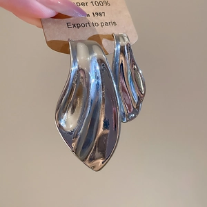 Macro detail of asymmetric liquid metal fishtail earrings in polished silver finish