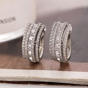 Silver huggie hoop earrings with cubic zirconia baguettes on a rustic wooden surface